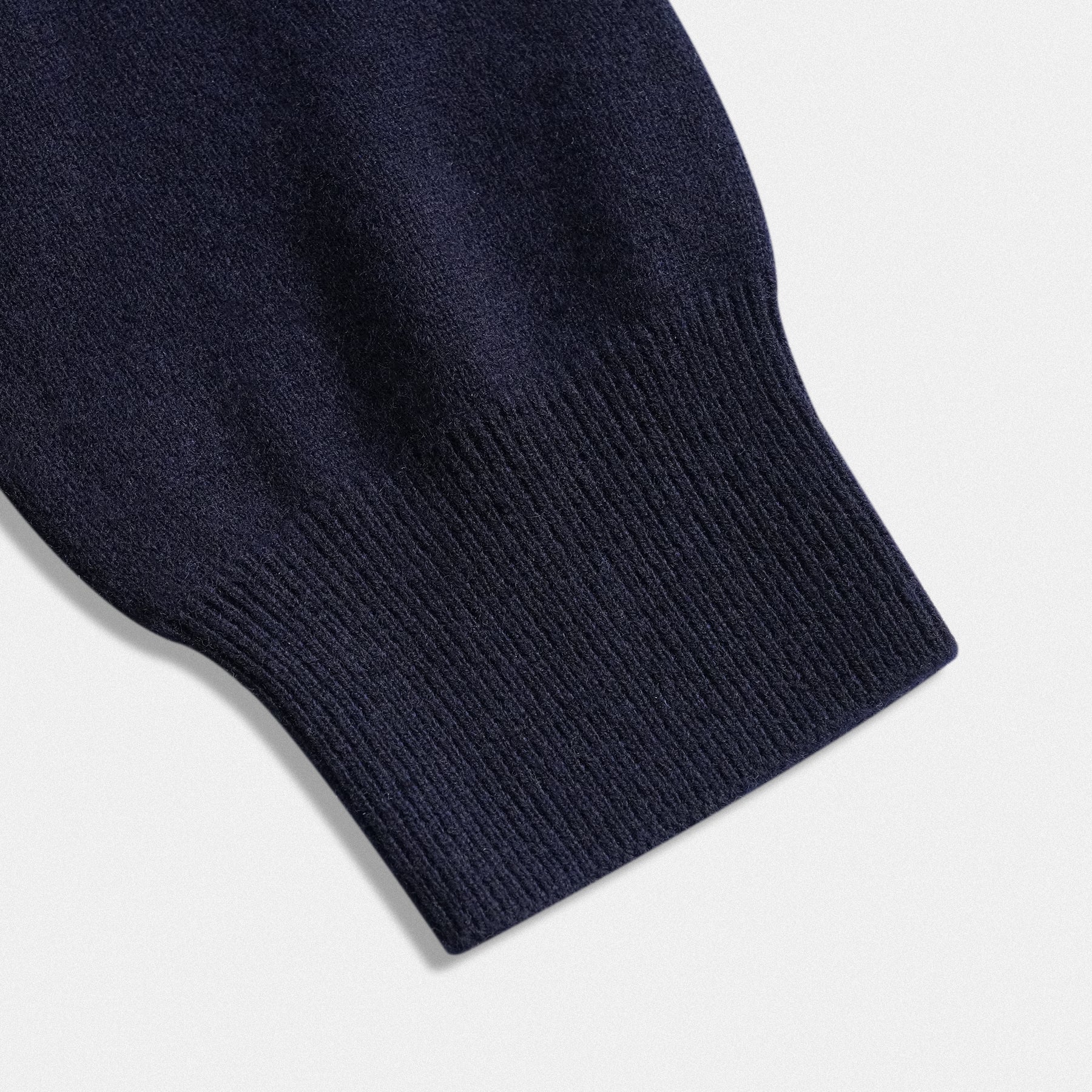 Dettaglio fondo manica scollo a V del pullover in lana 100% con applicazione cuore in tessuto rosso vino